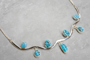 Silver necklace with turquoise stones on a gray surface