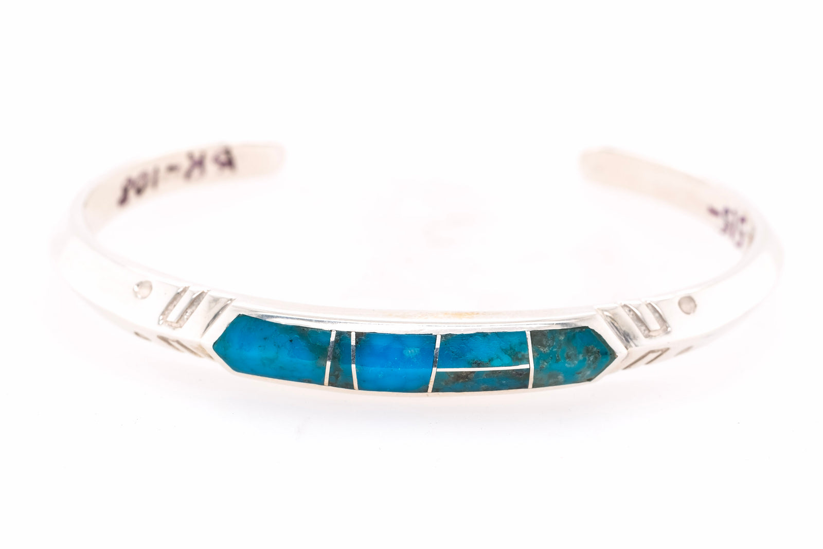 A sterling silver cuff bracelet featuring a central inlay of vibrant turquoise blue stones, photographed against a seamless white background.
