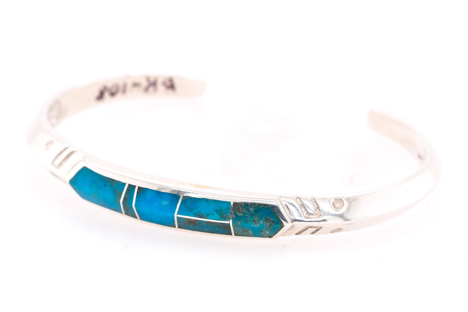 A sterling silver cuff bracelet featuring a central inlay of vibrant turquoise blue stones, photographed against a seamless white background.