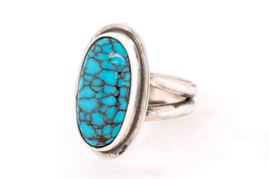 A sterling silver ring featuring an oval turquoise cabochon with a distinctive brown matrix pattern, set against a plain white background.