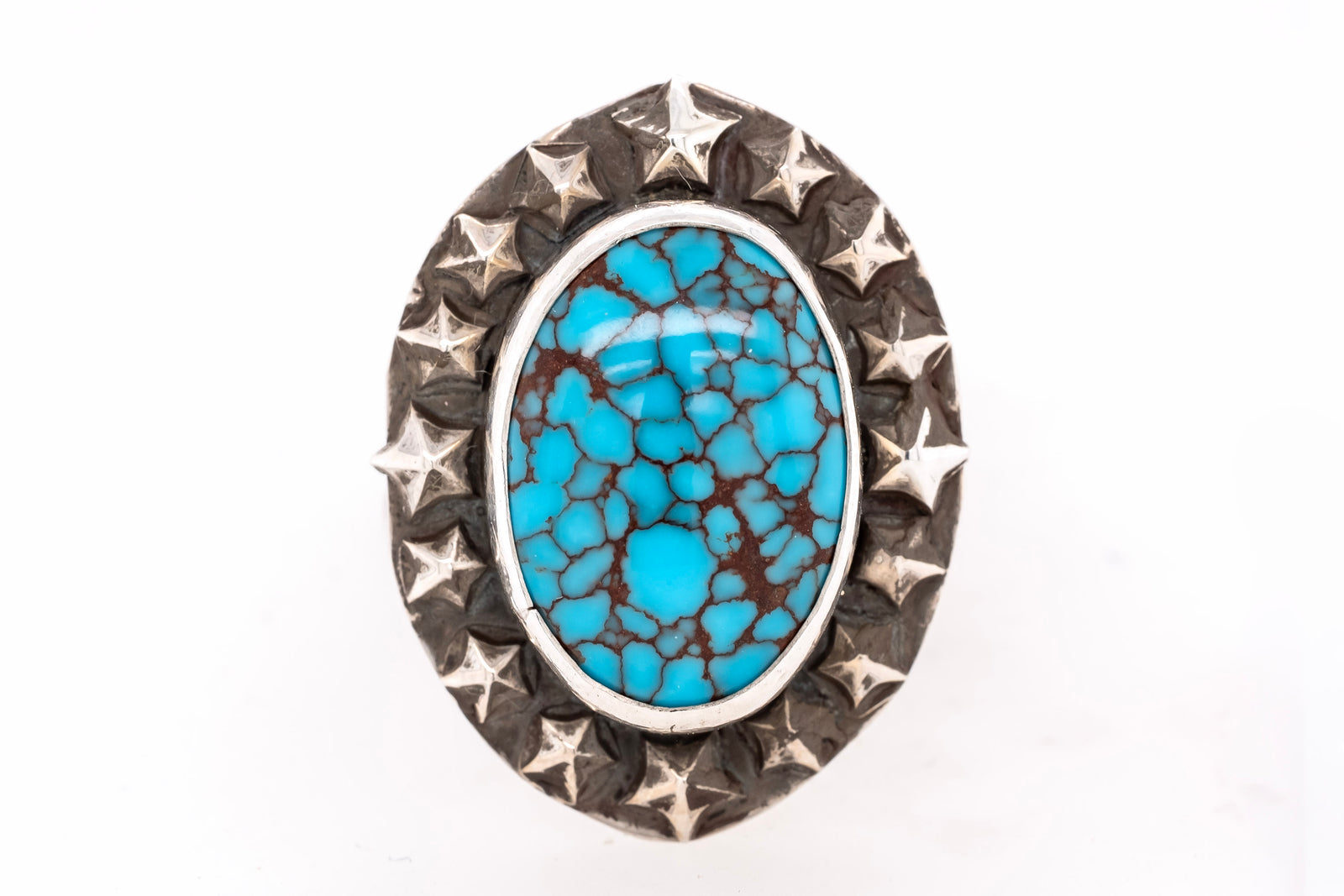 A silver ring featuring a large oval turquoise stone with brown matrix veining, surrounded by a textured silver border with star-like details.