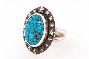 A silver ring featuring a large oval turquoise stone with brown matrix veining, surrounded by a textured silver border with star-like details.