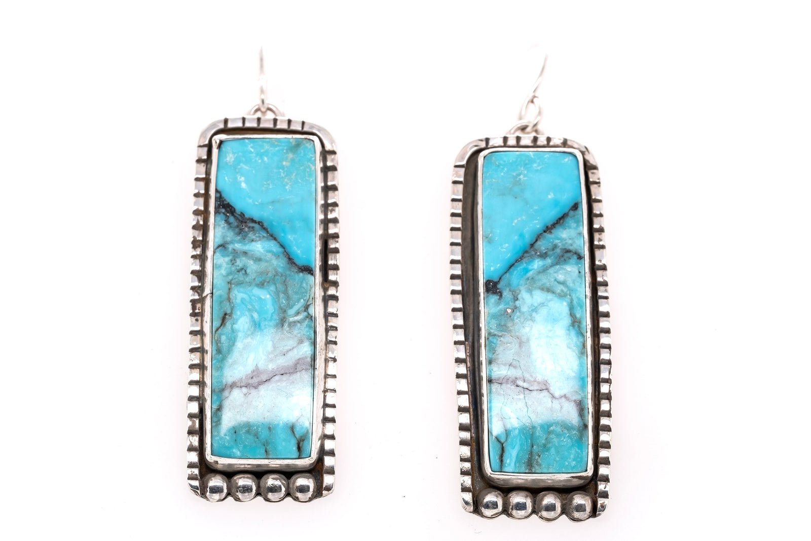 A pair of rectangular drop earrings featuring natural turquoise stones with silver bezel settings and dangling hooks, shown against a plain white background.