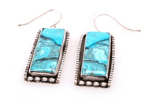 A pair of rectangular drop earrings featuring vibrant turquoise blue marbled stones set in textured silver bezels with fishhook wires, shown on a plain white background.