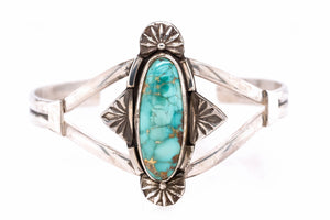 A sterling silver cuff bracelet featuring a central oval turquoise stone with gold flecks, surrounded by decorative starburst and diamond-shaped silver settings.