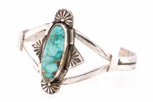A sterling silver cuff bracelet featuring a prominent oval turquoise stone with brown matrix veining, accented by decorative sunburst and leaf motifs on a white background.