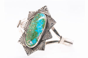 A sterling silver cuff bracelet featuring a large, oval-shaped turquoise stone with green and blue matrix patterns, set against a clean white background.