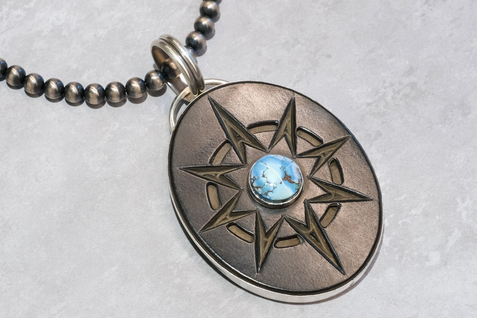 Handmade Golden Hills Turquoise pendant by Skylar Glandon with carved Richlite compass design, silver bezel, and large bail for Navajo Pearls