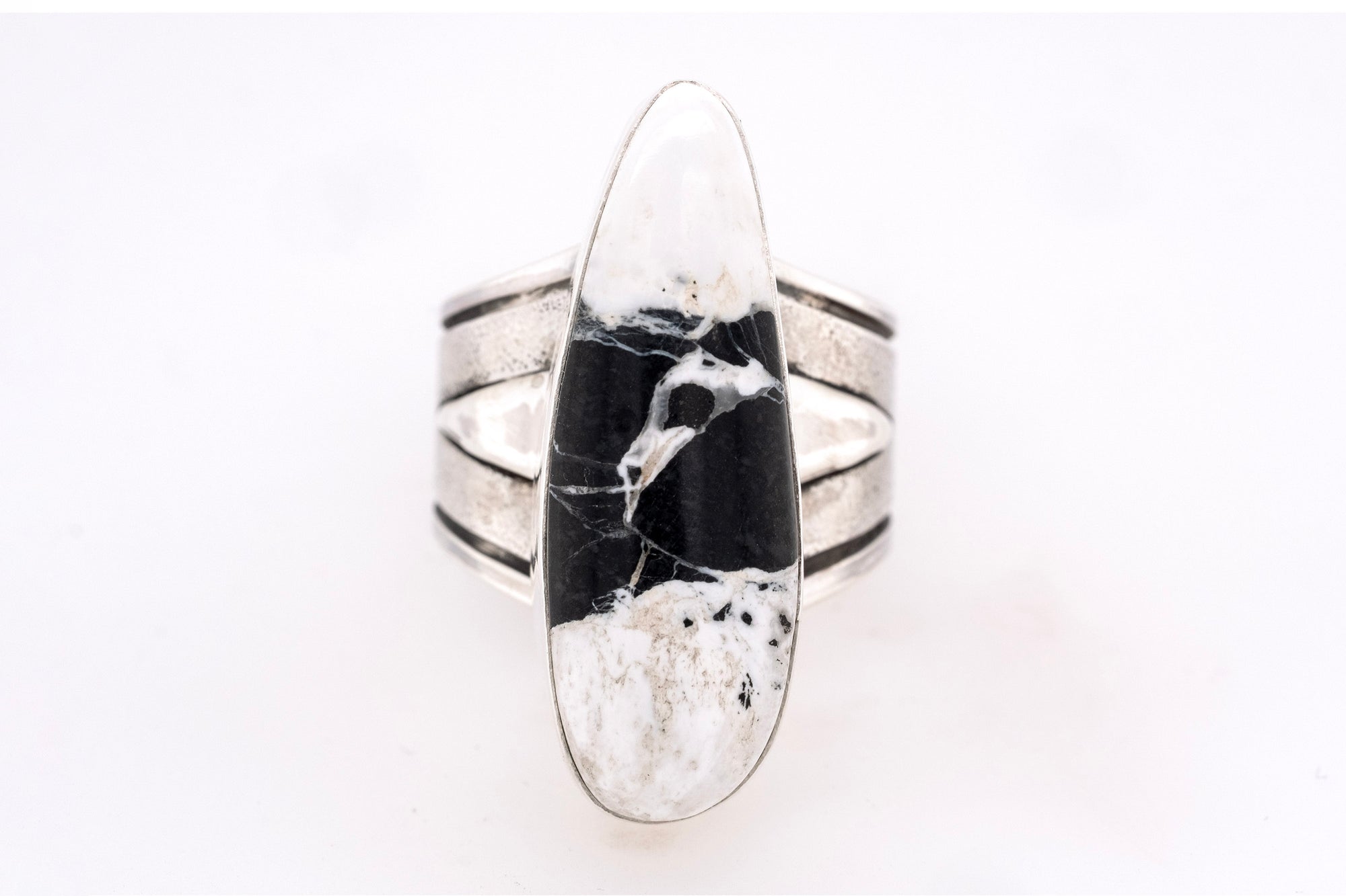 Handmade sterling silver ring with elongated White Buffalo stone in black and white, textured band, and triangular silver accents by Skylar Glandon